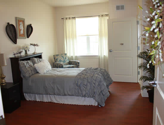 A cozy bedroom with a neatly made bed, an armchair, and a window letting in natural light.