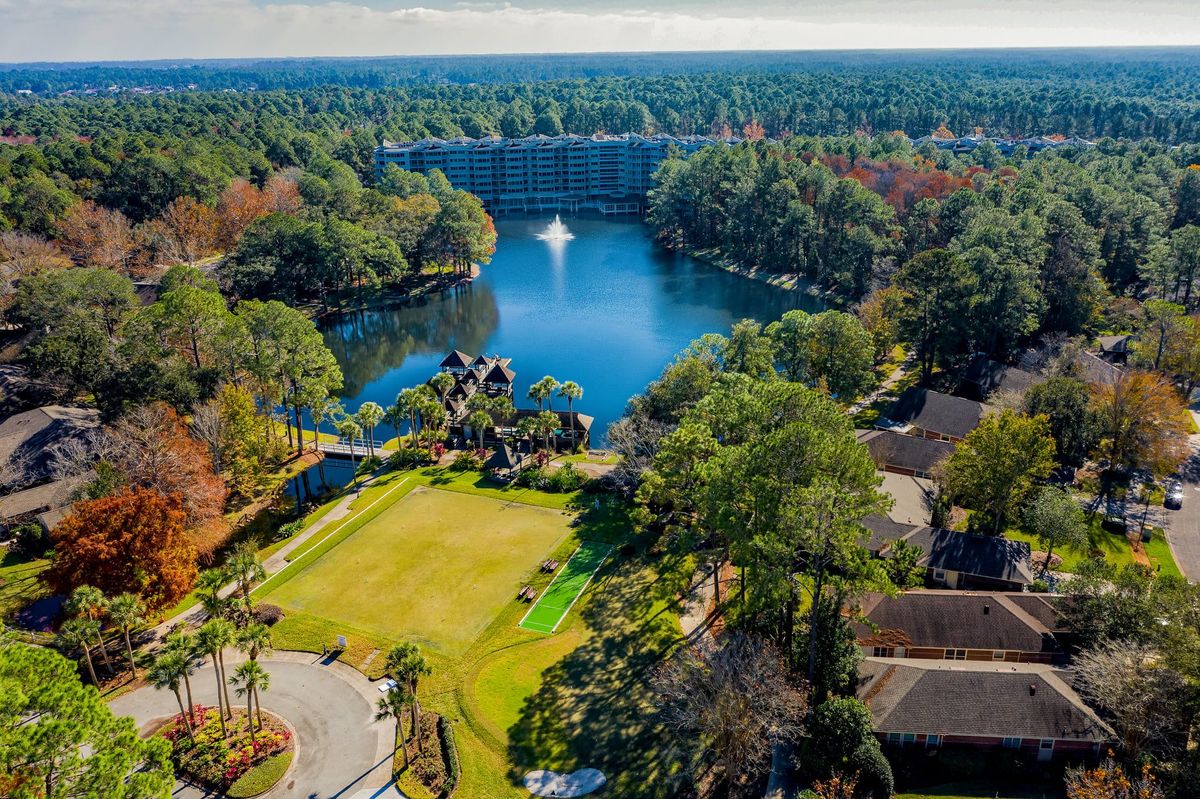 A serene aerial view of a lake with a fountain surrounded by lush greenery and buildings.
