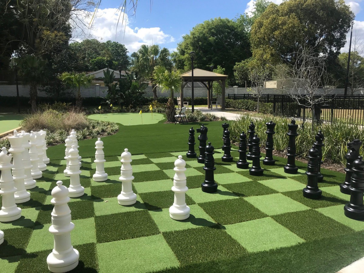 A large outdoor chess set in a garden with a gazebo and surrounding trees.