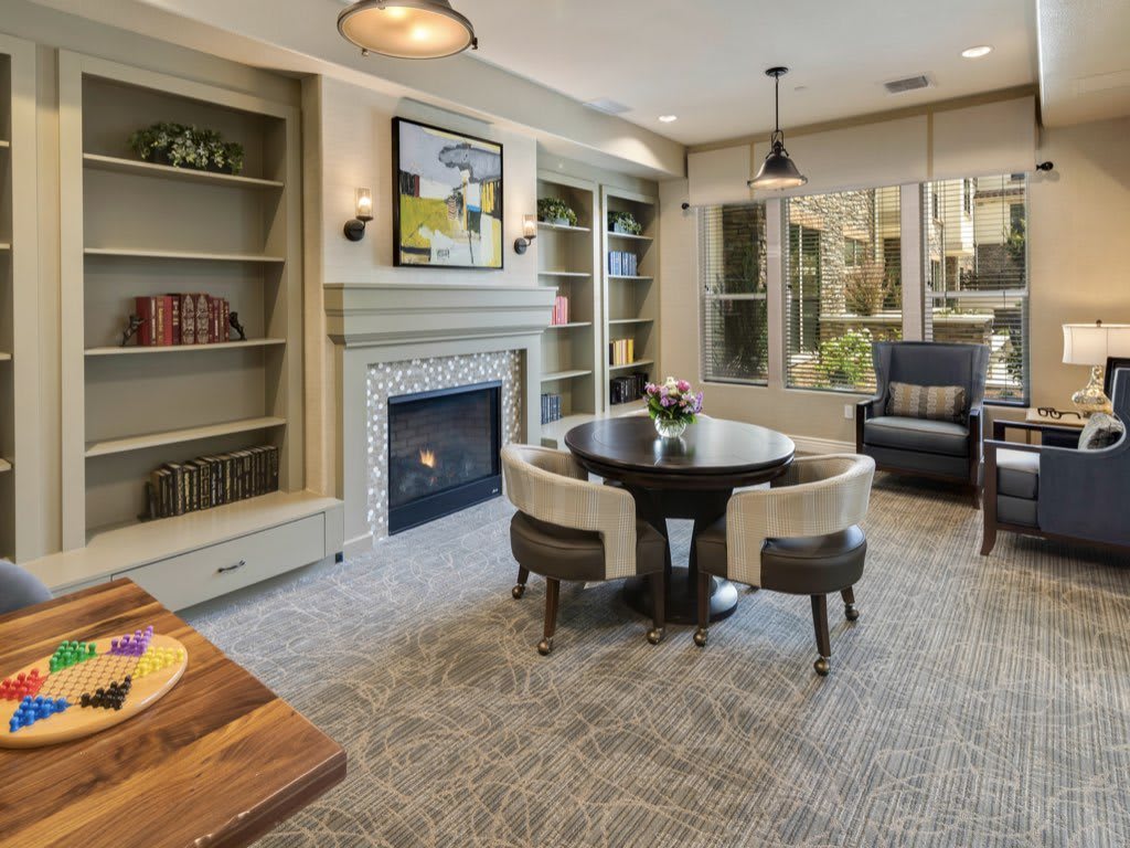 A cozy living room with a fireplace, surrounded by bookshelves and a central table with chairs.