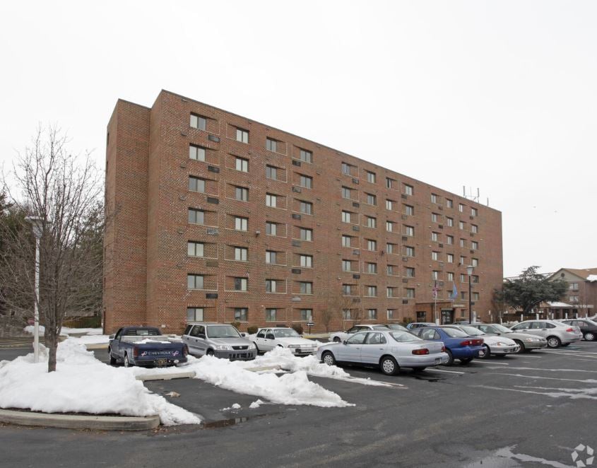 A multi-story brick apartment building with a snow-covered parking lot and several parked cars.