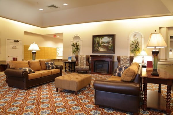 A cozy living room featuring comfortable sofas, a central ottoman, and a fireplace, with warm lighting and decorative elements.