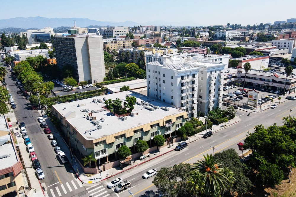 Aerial view of a cityscape featuring multiple buildings, streets, and traffic with trees lining the roads.