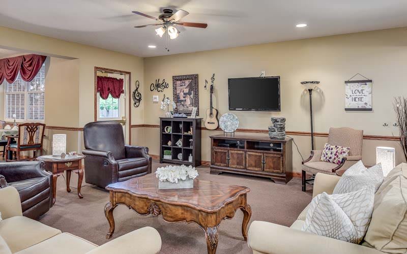 A cozy living room with a mix of traditional and modern decor, featuring a television, armchairs, sofas, a coffee table, and decorative items including a guitar.