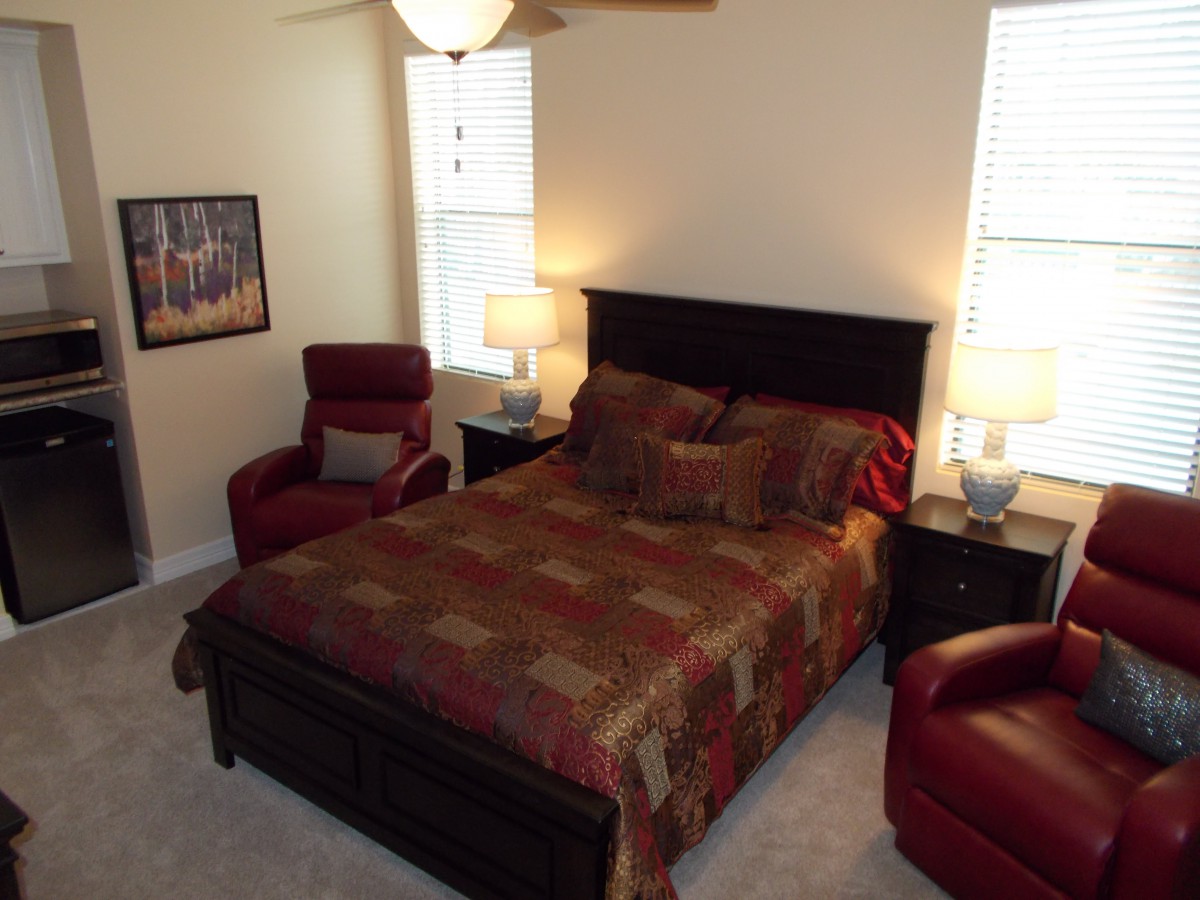 A cozy bedroom with a bed, two armchairs, and warm lighting.