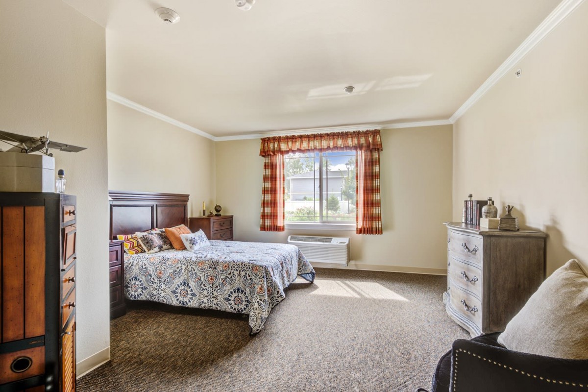 A cozy bedroom with a bed, dresser, and a window letting in natural light.