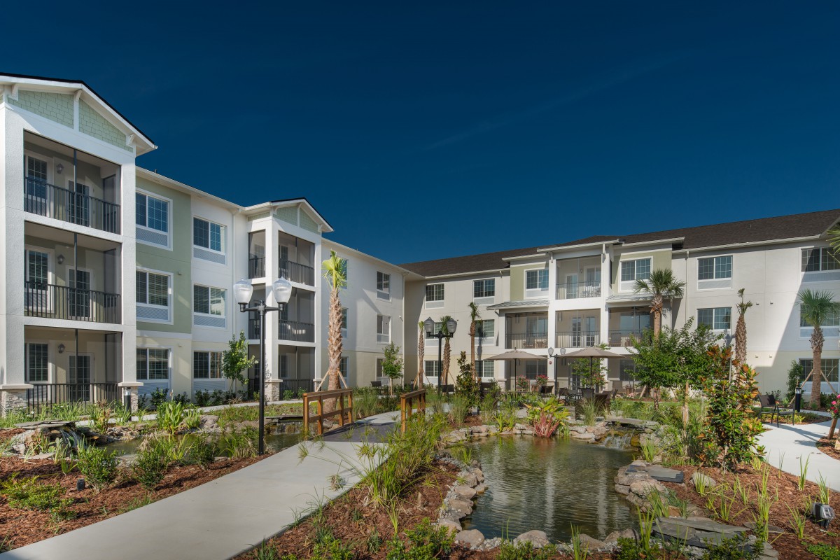 A modern apartment complex with landscaped gardens and a pond.