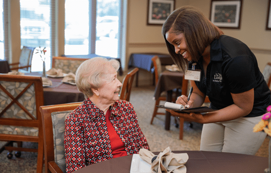A caregiver happily interacting with an elderly woman in a comfortable indoor setting.