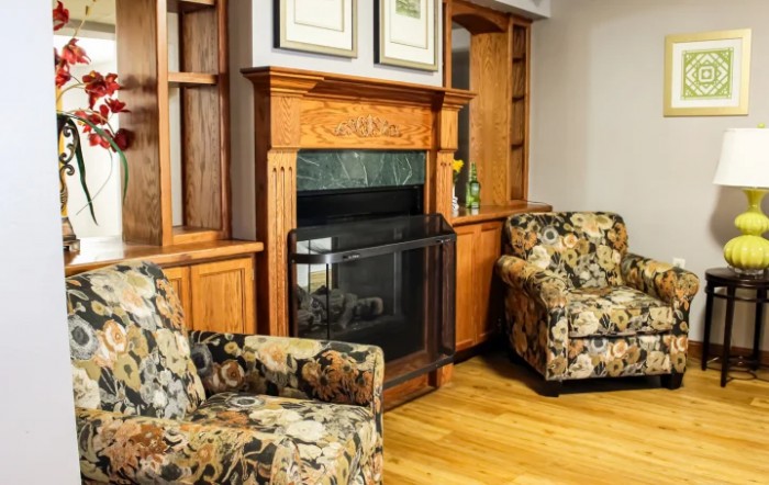 A cozy living room with a wooden fireplace and floral armchairs.