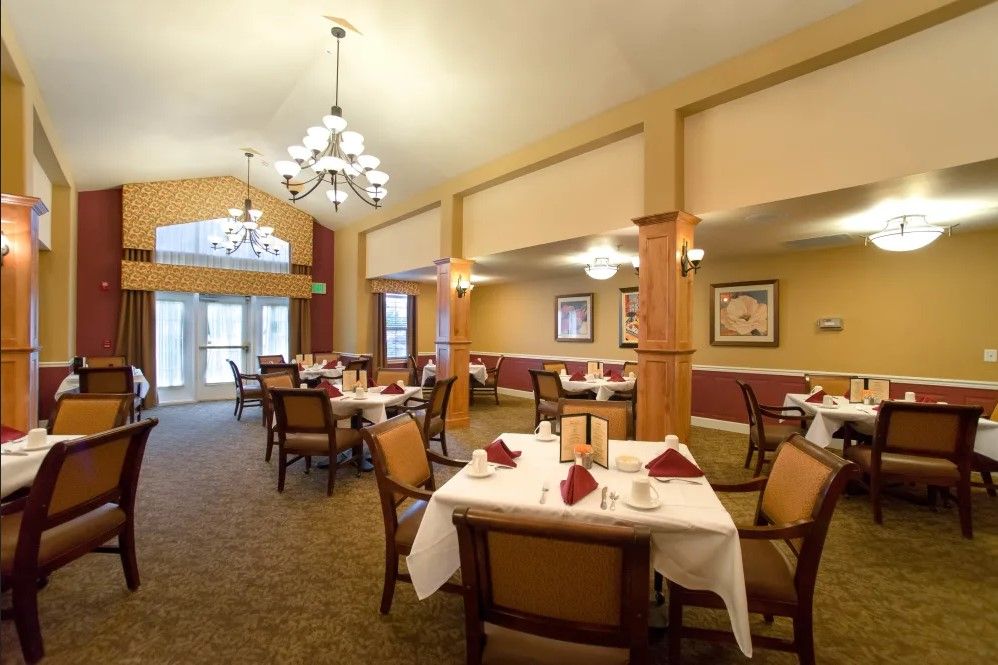 An elegant dining room with neatly arranged tables and chairs, well-lit by chandeliers.