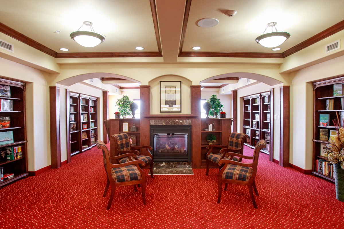 A cozy library with a fireplace, surrounded by bookshelves and a seating area on red carpet.