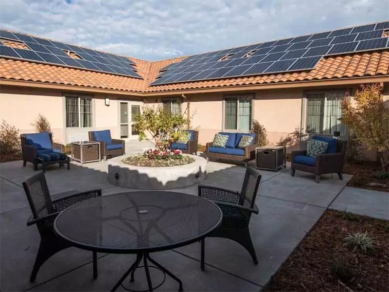 A courtyard featuring outdoor seating and tables, with solar panels installed on the rooftop under a clear sky.