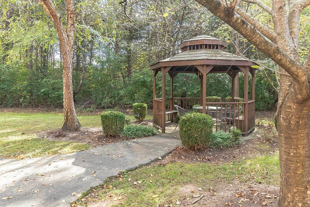 A peaceful garden setting with a wooden gazebo surrounded by trees and greenery.