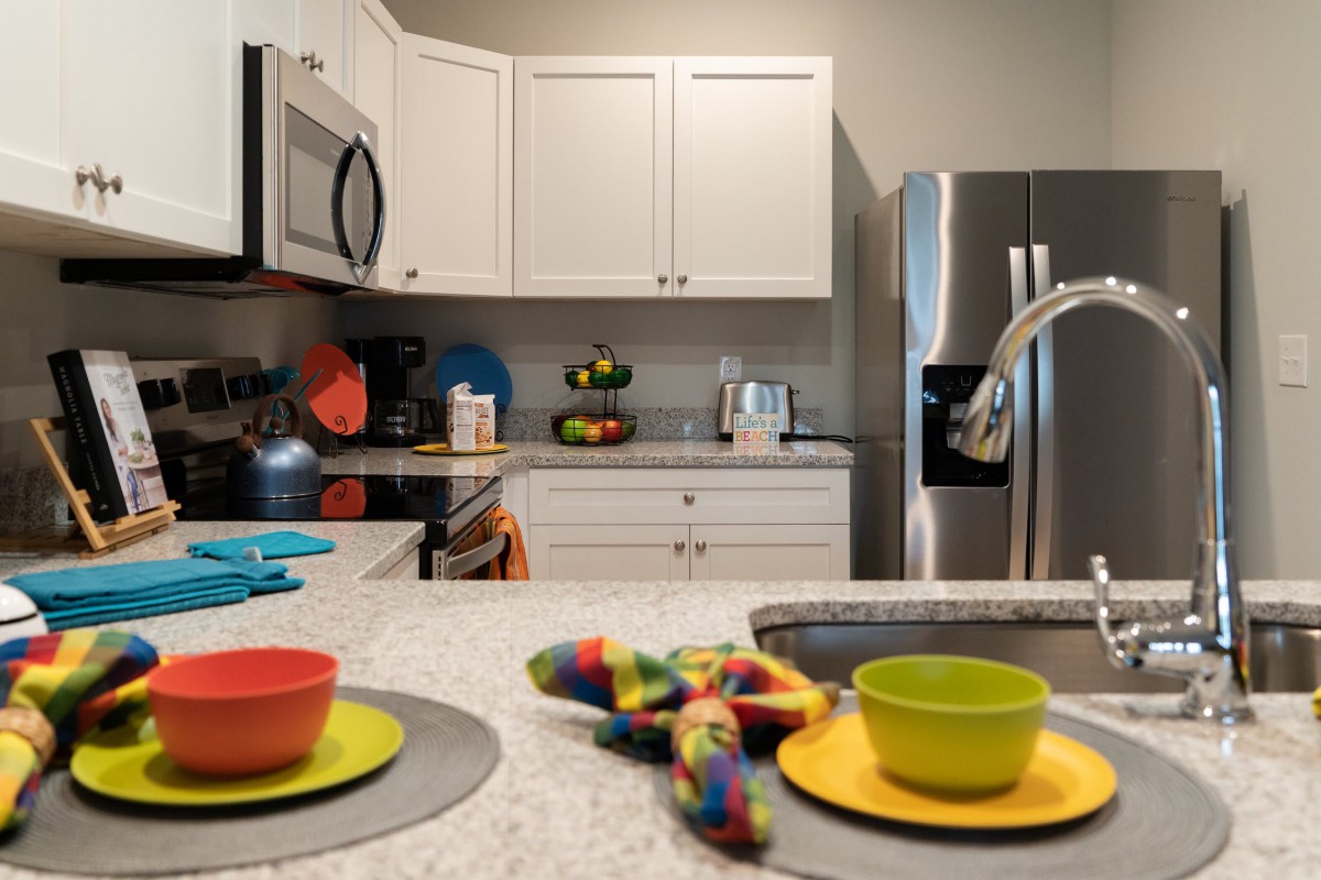 A modern kitchen interior with white cabinets, stainless steel appliances, and colorful dishes on the countertop.