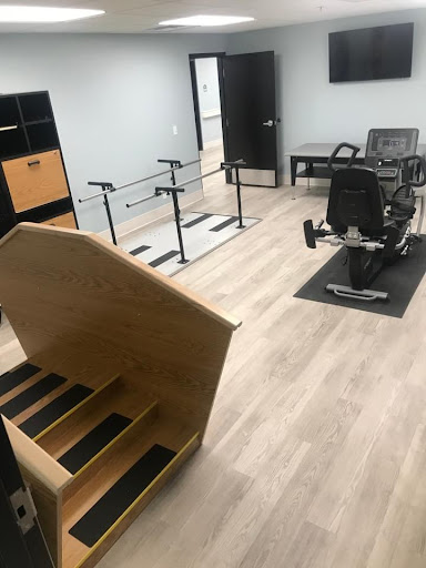 A spacious physical therapy room equipped with stairs, parallel bars, and exercise equipment.