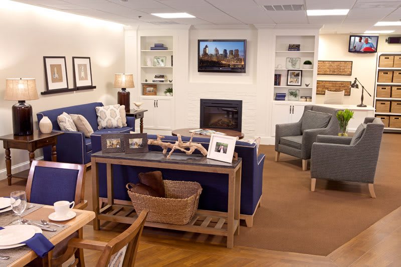 A cozy living room with sofas, chairs, and a television above the fireplace surrounded by shelves.