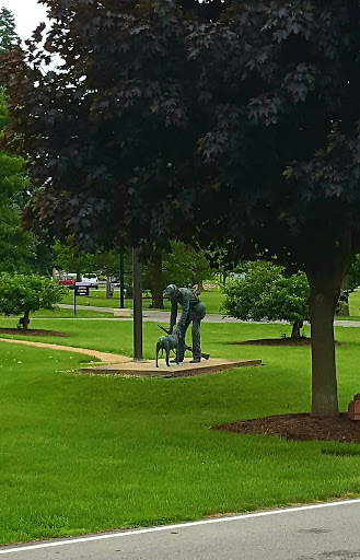 A tranquil park scene featuring a sculpture of a person and a dog, surrounded by lush greenery.