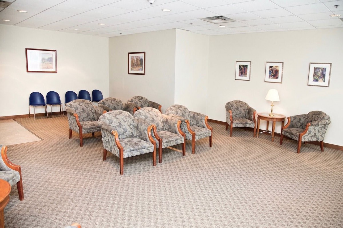 A waiting room with rows of upholstered chairs and framed pictures on the walls.