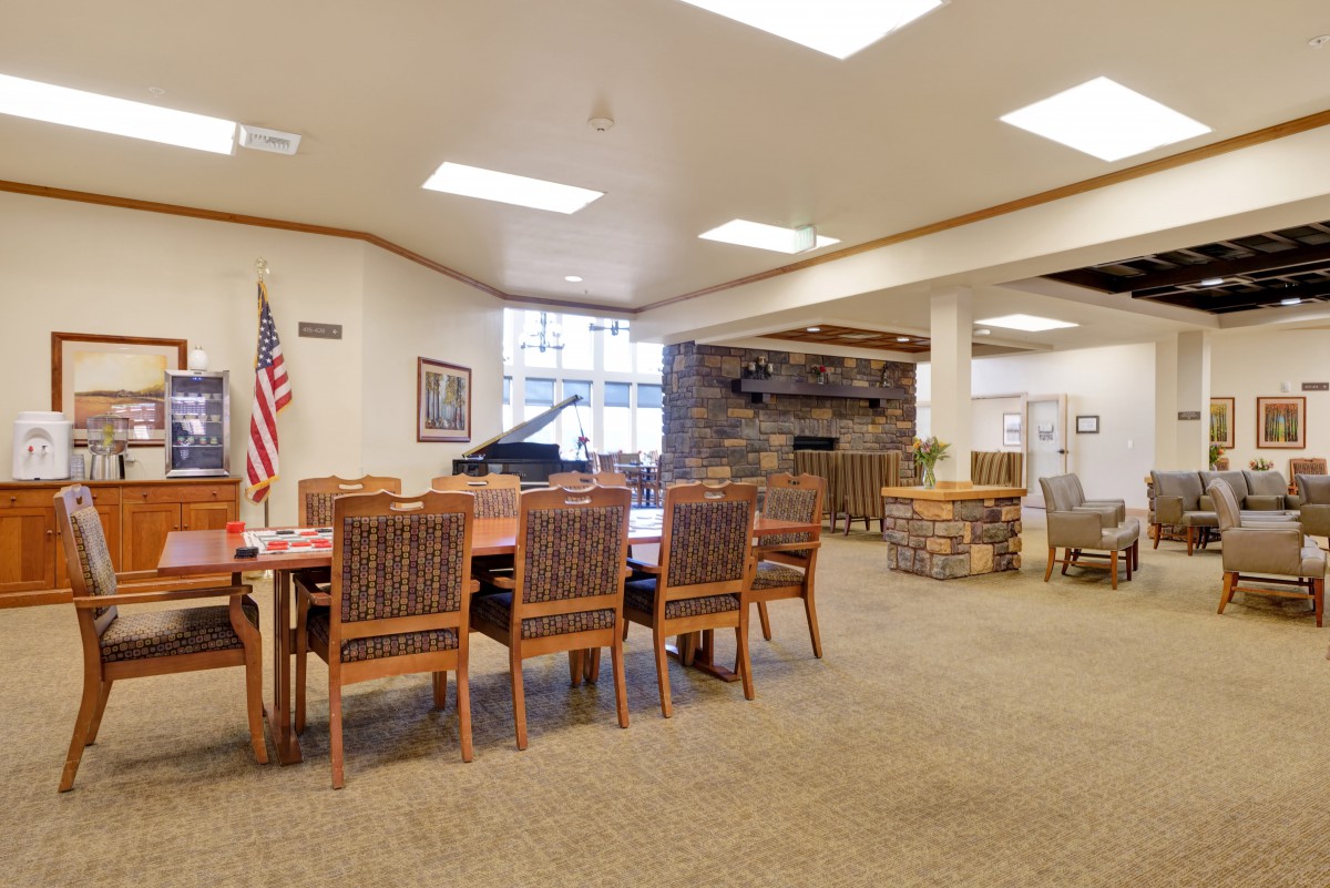 A cozy library interior with a large table and chairs, surrounded by bookshelves and a flag in the corner.