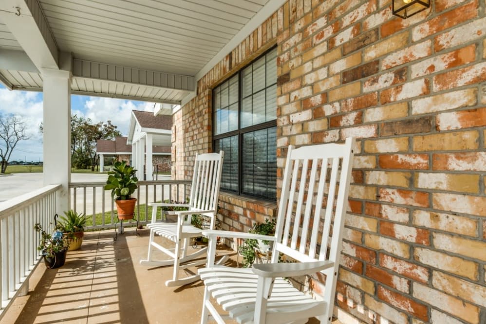 A cozy front porch with white rocking chairs against a brick wall.