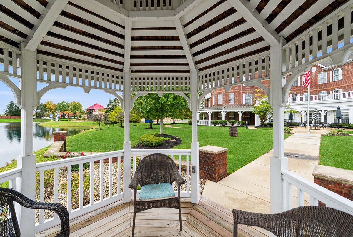 A scenic view from inside a wooden gazebo overlooking a lush garden and brick building.