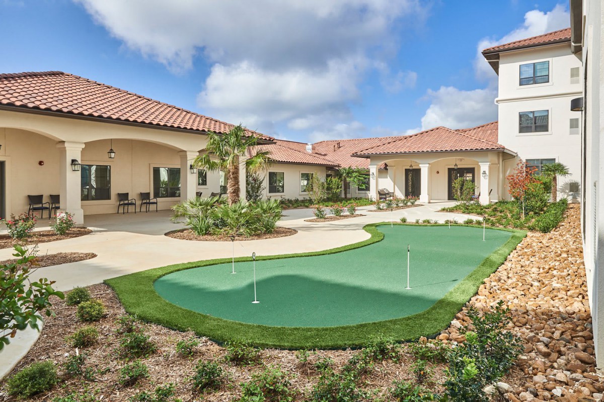 A courtyard with a putting green and landscaped areas surrounded by residential buildings on a sunny day.