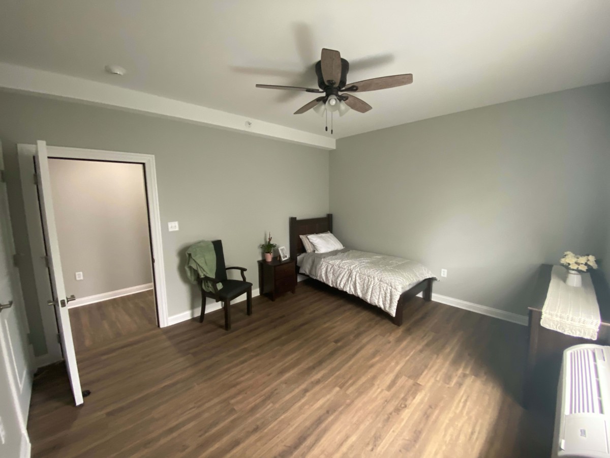 A minimalist bedroom with a single bed, wooden floors, and a ceiling fan.