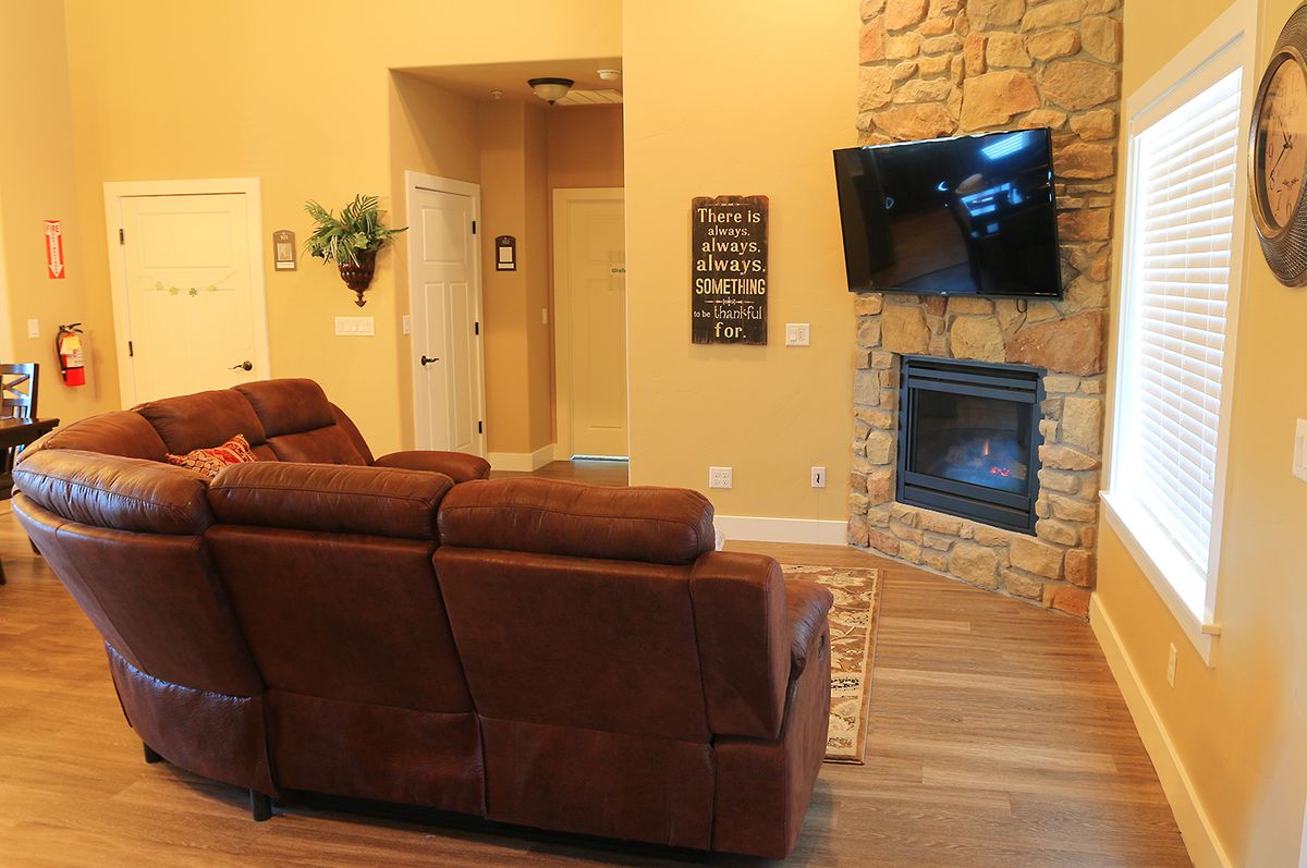 A cozy living room featuring a brown sofa, stone fireplace, and a wall-mounted television.