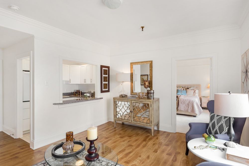 A cozy living room with wood flooring, featuring stylish furniture and an open view of the kitchen.