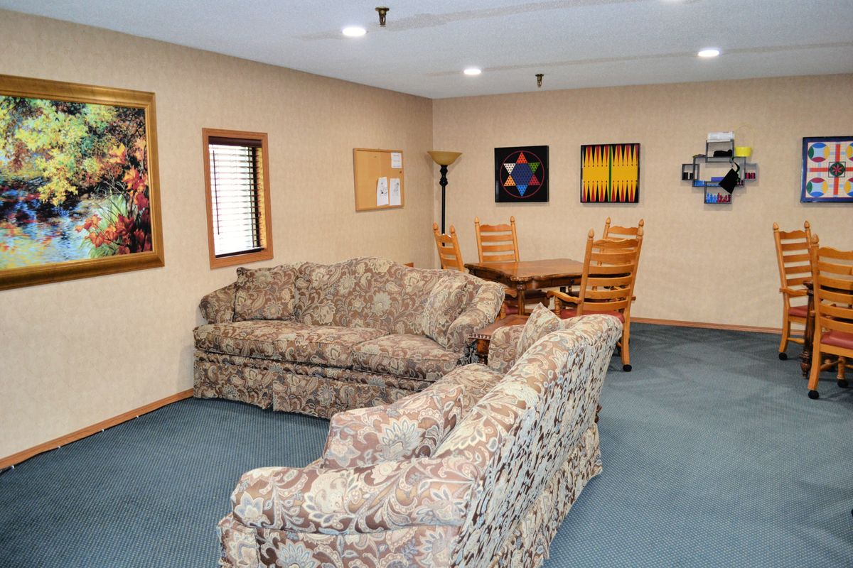 A cozy living room with floral-patterned sofas, a wooden dining table and chairs, decorated with artwork on the walls.