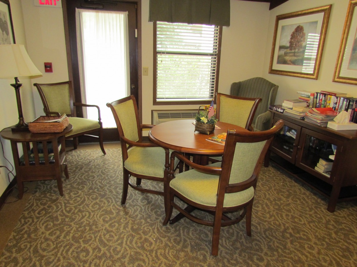 A cozy living room with a round table and chairs, soft lighting, and a carpeted floor.