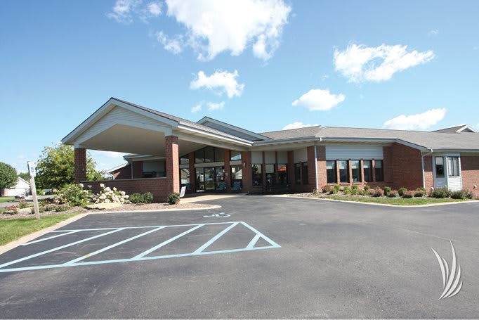 A modern building with a covered entrance and adjacent parking lot under a partly cloudy sky.
