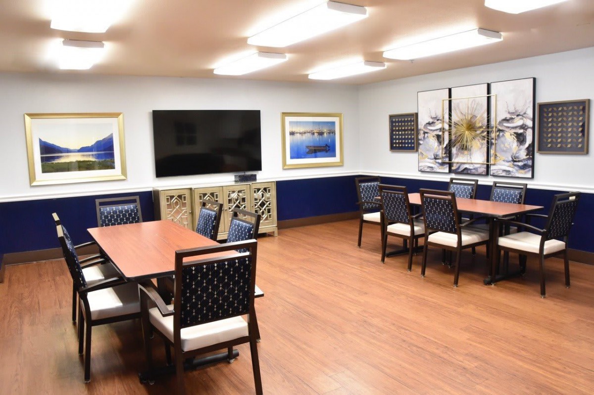 A modern meeting room with tables, chairs, a large television, and wall art.