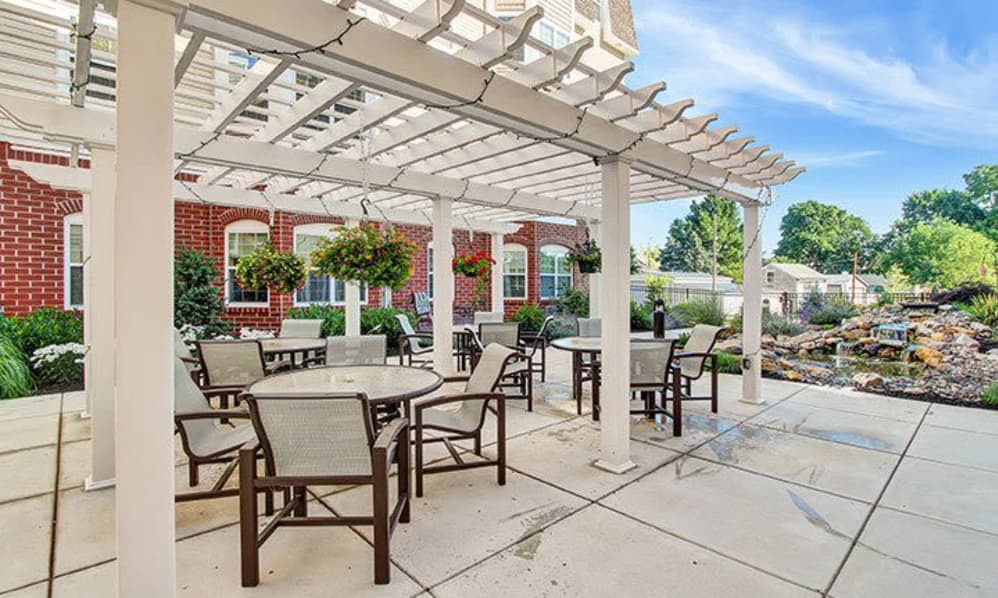 An inviting outdoor patio area with a pergola, featuring tables and chairs surrounded by hanging plants and a brick building background.