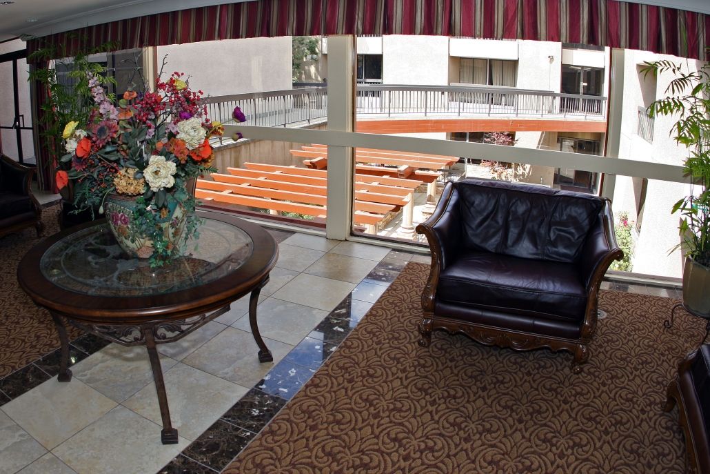 A lobby area with a leather chair and a table adorned with a flower arrangement, overlooking a window view.