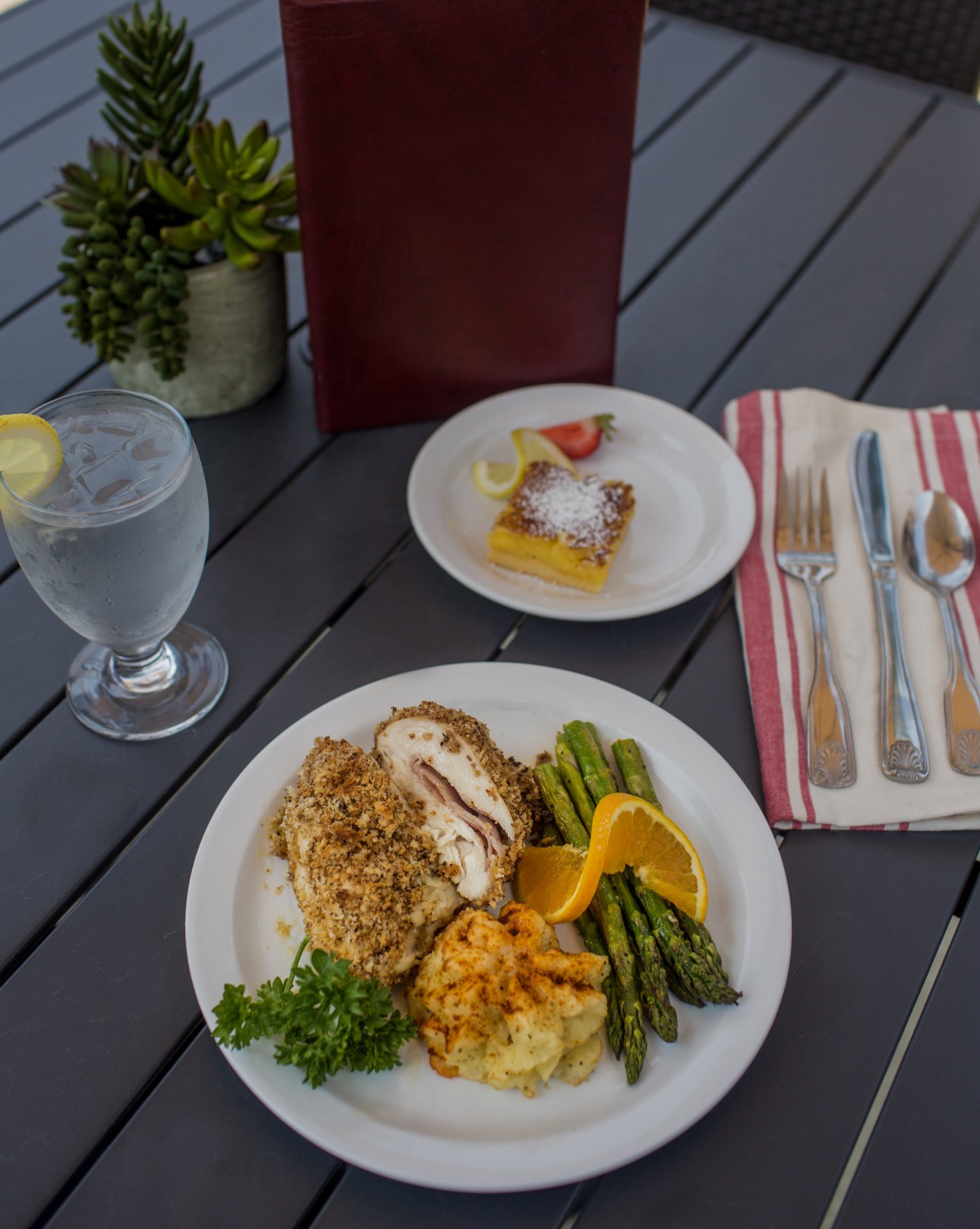 A delicious meal featuring chicken with mashed potatoes and asparagus, accompanied by a dessert and a glass of water with lemon.