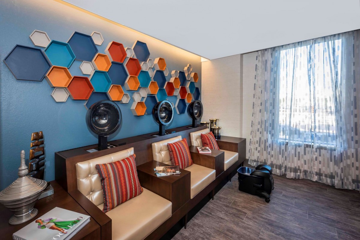 A modern salon seating area with colorful hexagonal wall art and built-in hair dryers.