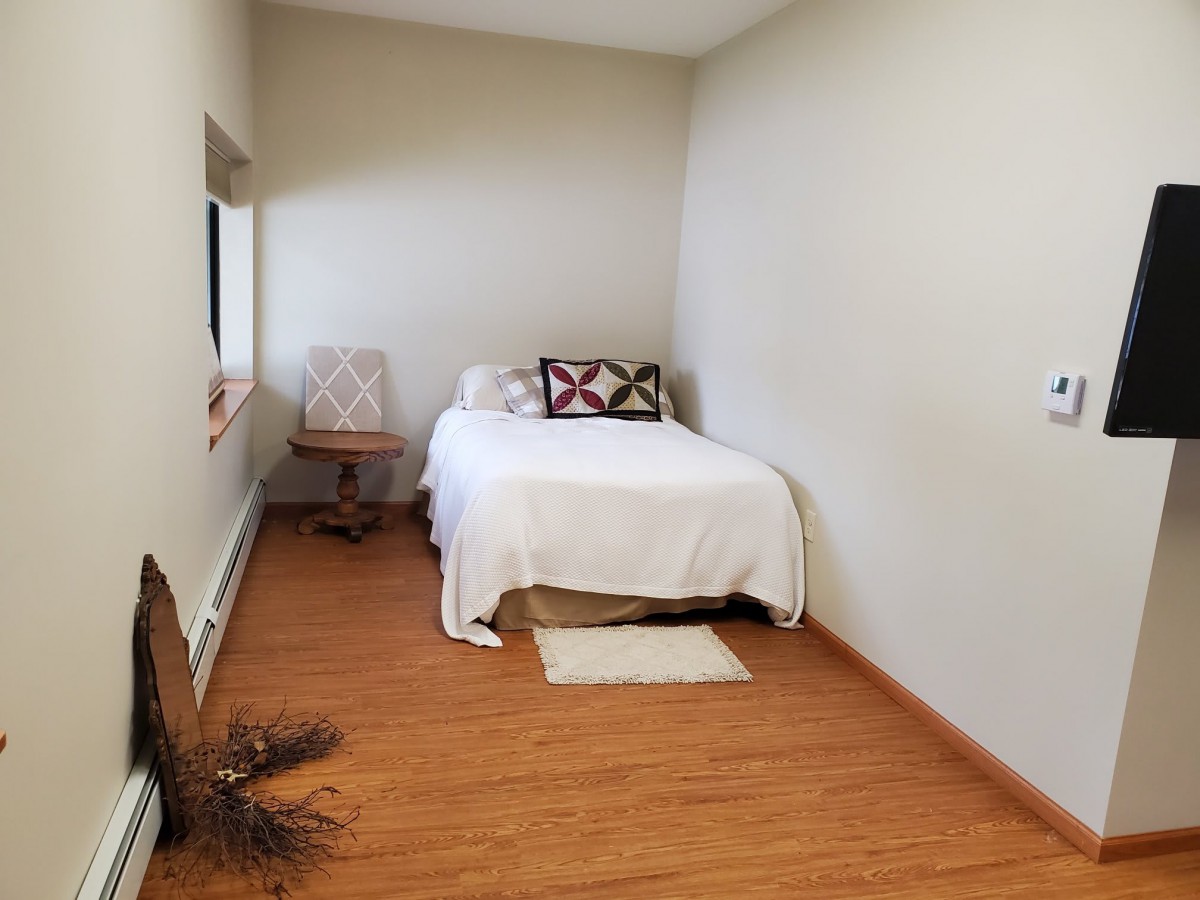 A minimalist bedroom with a single bed, chair, and wooden flooring.