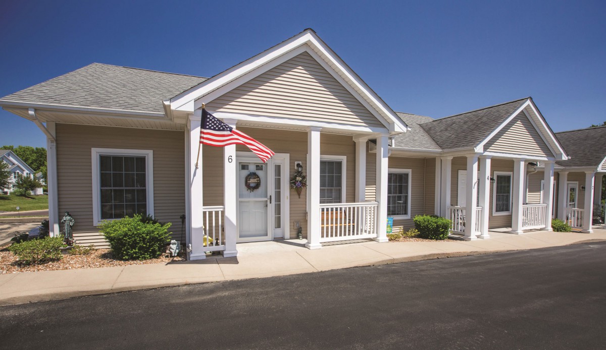 A charming colonial-style house with an American flag displayed on the porch under a clear blue sky.