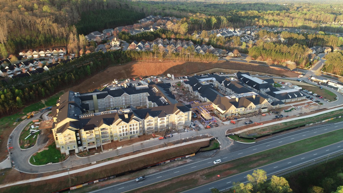 Aerial view of a residential area under construction with nearby roads and wooded surroundings.