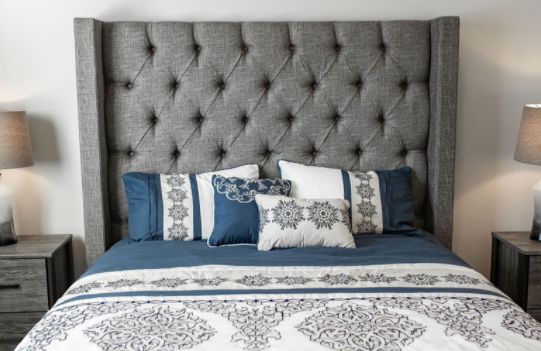 A bed with a tufted gray headboard and blue and white bedding.