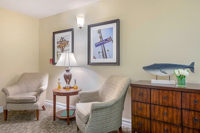 A cozy living room corner with two chairs, a lamp on a side table, and framed artwork on the wall.