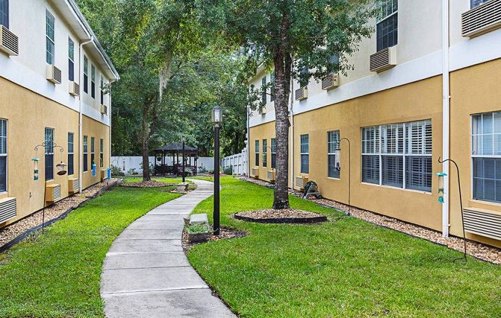 A scenic view of an apartment complex featuring a curved pathway surrounded by lush greenery and trees.