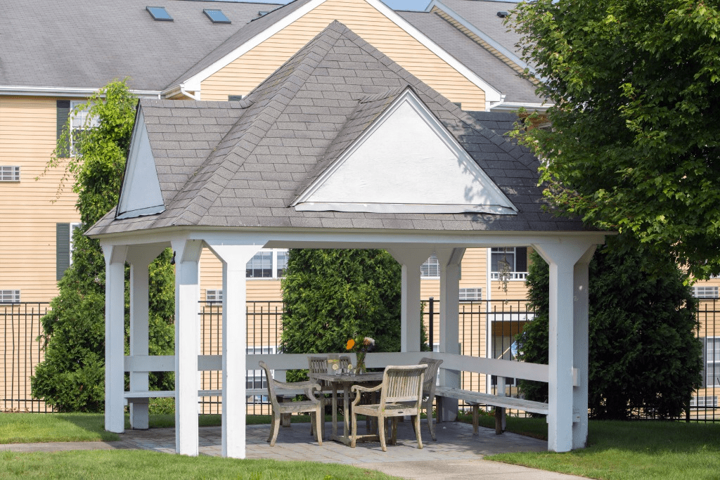A wooden gazebo with outdoor furniture situated in a sunny garden area.
