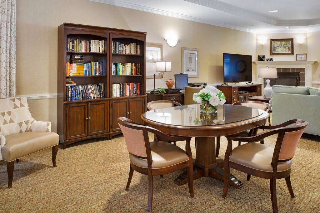 A cozy library room with bookshelves and a round table surrounded by chairs.