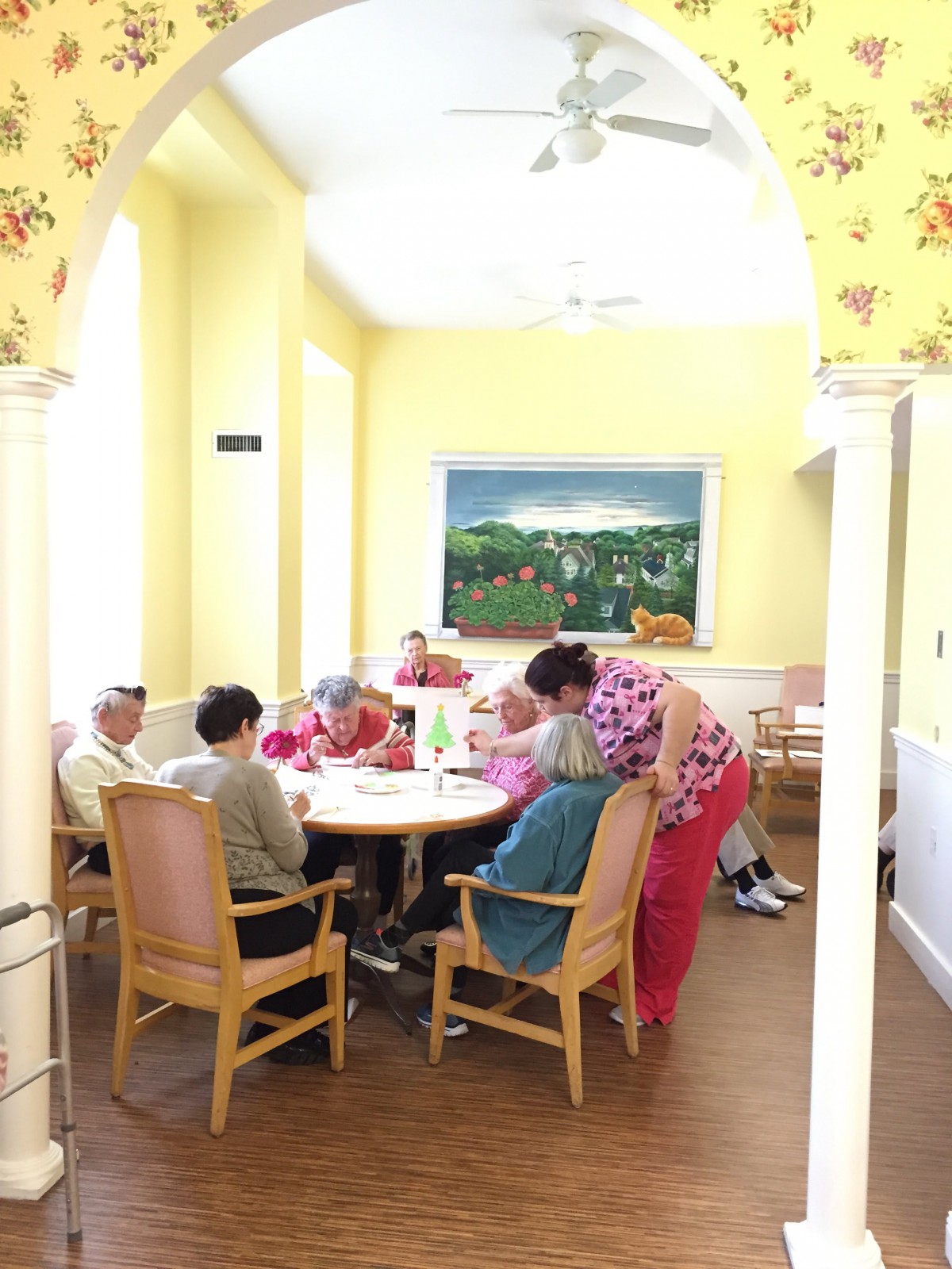 A group of elderly individuals seated around a table in a brightly lit room, engaged in conversation or activities.