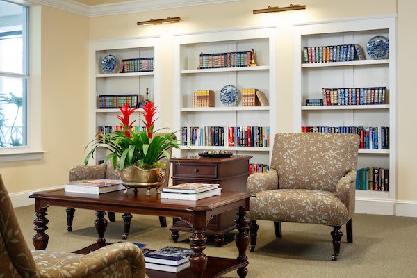 A cozy library room with bookshelves, armchairs, and a coffee table adorned with a vibrant plant.