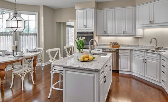 A modern kitchen with white cabinets, a central island with bar stools, and ample natural light.