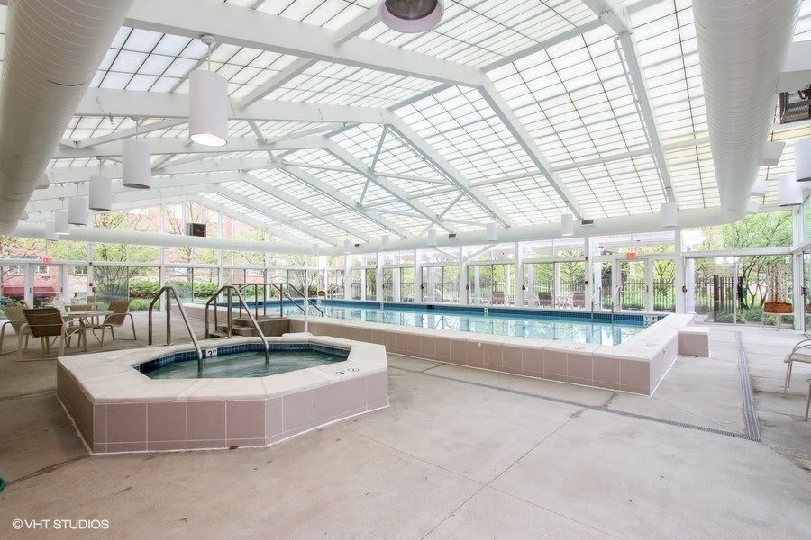 A modern indoor swimming facility featuring a glass ceiling with a pool and hot tub.