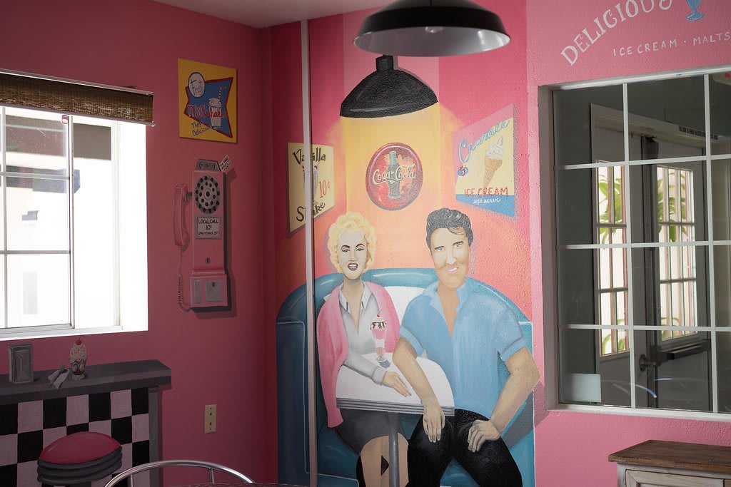 A retro-themed mural inside a diner with pink walls, depicting two people in 1950s attire.